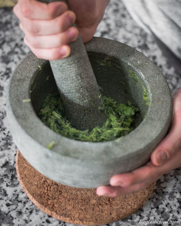 A photo of some bashing a bunch of ingredients into a paste in a pestle mortar.