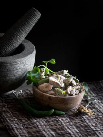 A dark, moody photo of green chicken curry served in a small bowl.