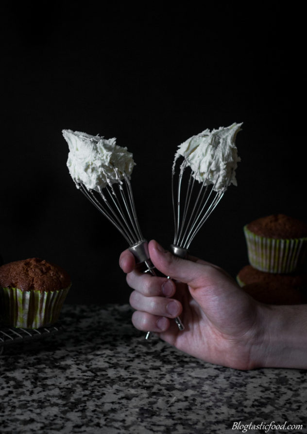 A photo of someone holding a couple of whisk attachments with butter-cream on them