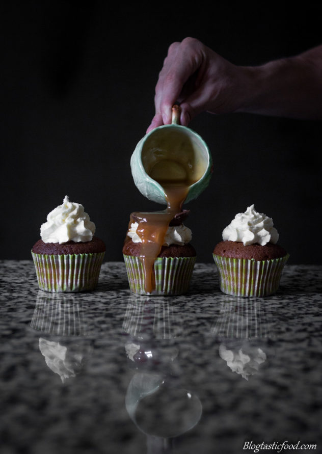 A photo of someone pouring caramel over one of three cupcakes.