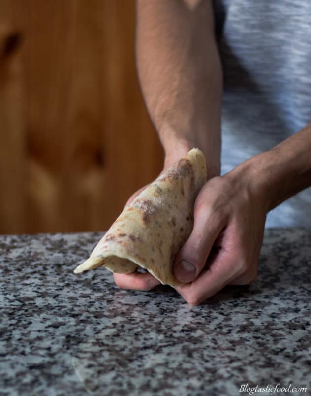A photo of someone using their hands to bed a piece of flatbread.