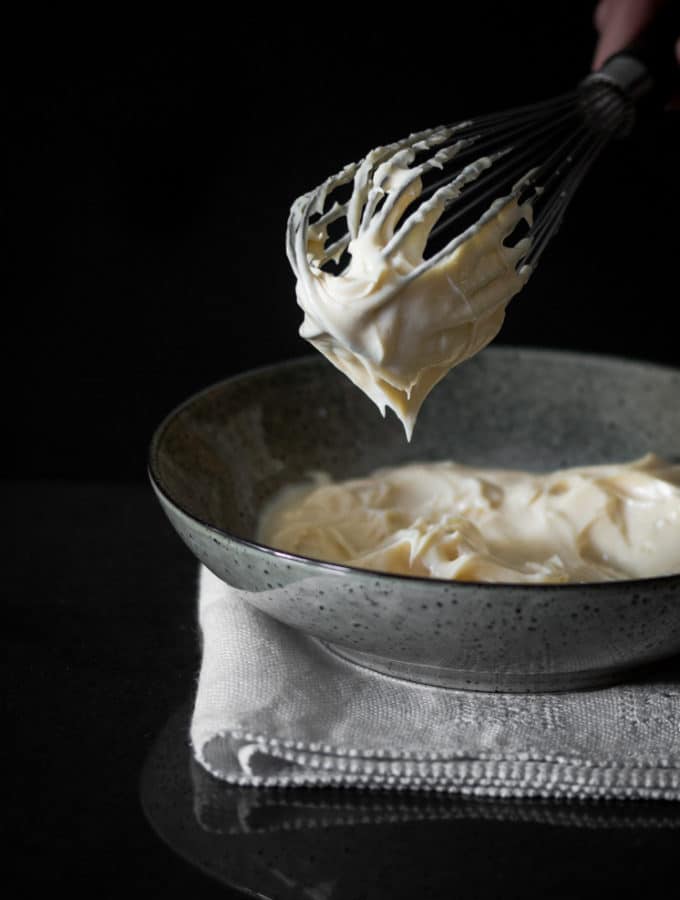 A photo of a whisk holding mayonnaise over a bowl.