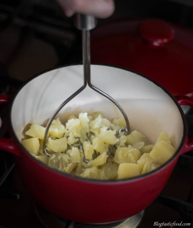 A photo of potatoes being mashed in a pot.