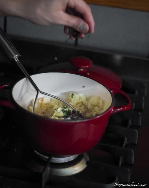 A photo of parsley getting sprinkled in a pot filled with potatoes.