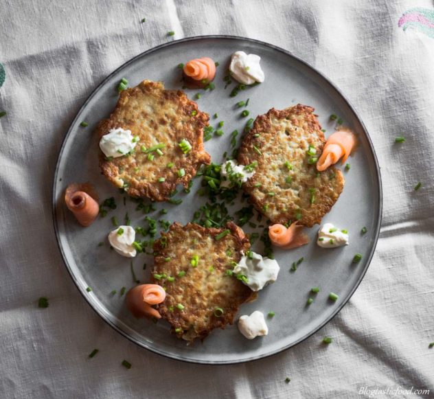 A plate of potato cakes with smoked salmon, sour cream and chives served in a fancy way on a plate. 