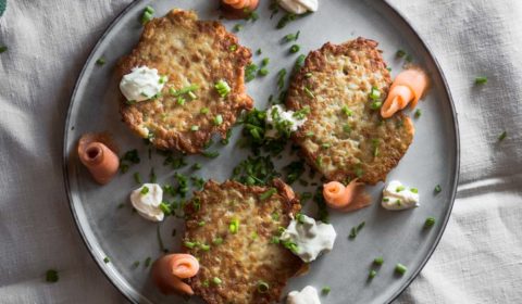 A overhead photo of potato cakes served with smoked salmon. And garnished wish sour cream and chives.