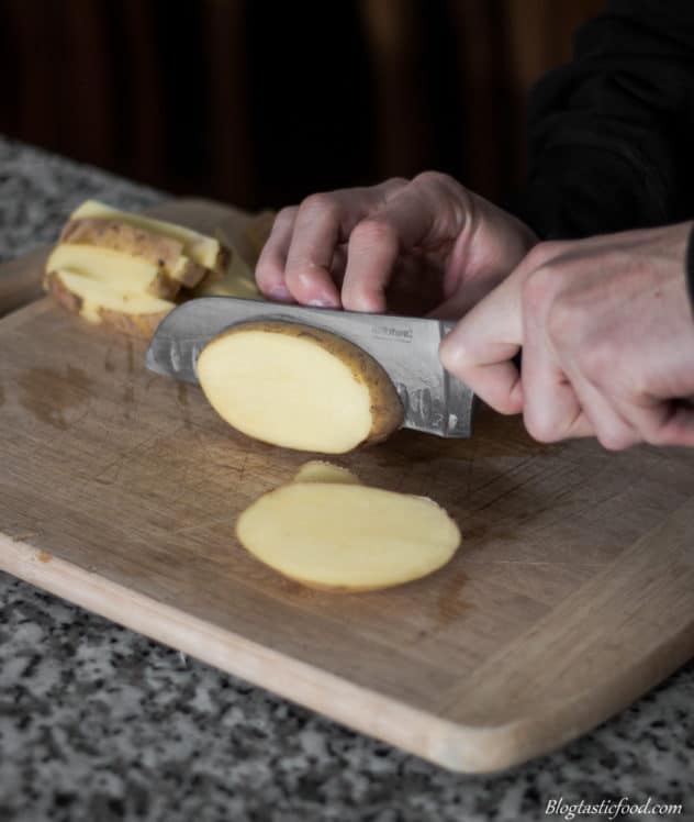 A photo of someone slicing a potato into disks.