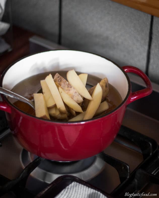 A photo of some using a slotted spoon of slowly plunge potatoes into a pot of hot oil.