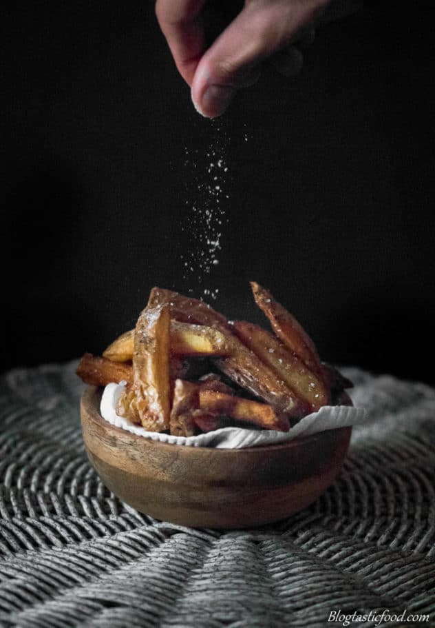 An eye level photo of someone sprinkling salt over a bowl of chips.