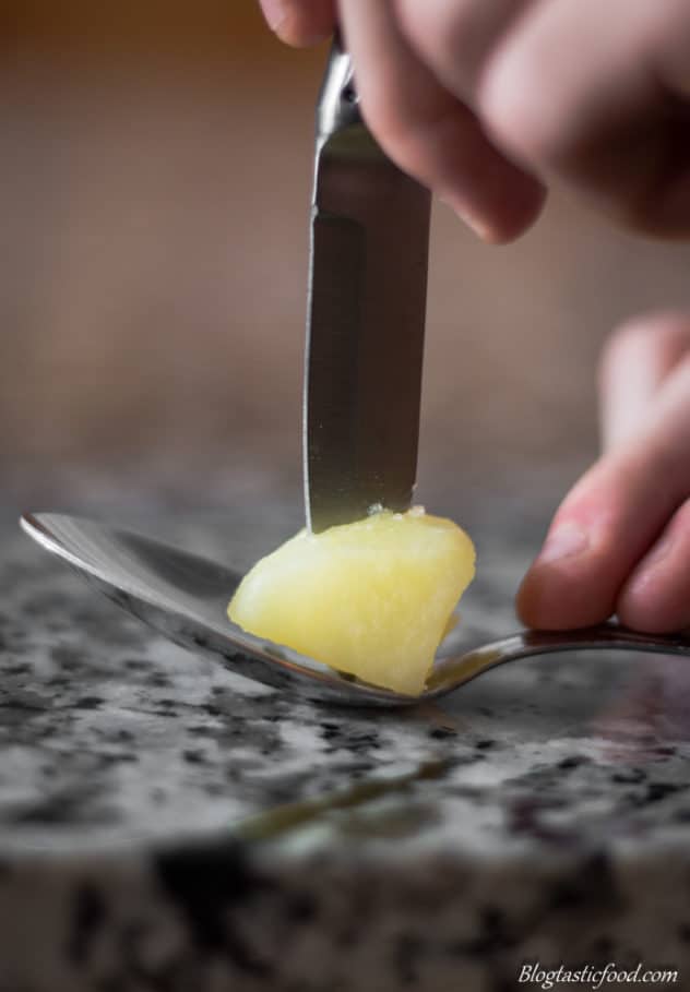 A photo of someone sticking a knife into a dice of boiled potato.
