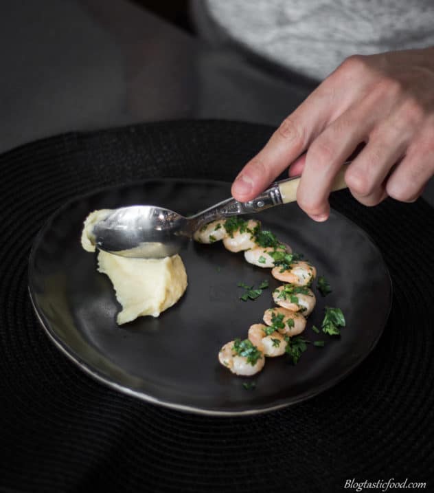 Potato puree being spooned into a plate with prawns on it.