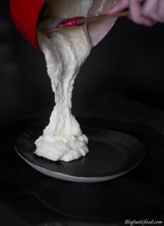 A photo of someone pouring potato puree onto a black plate.