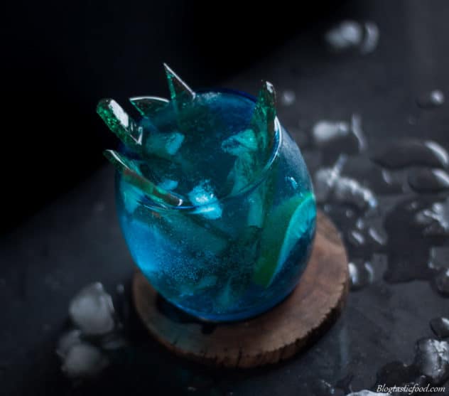 A Russian tilt photo of a blue cocktail with lemon and spikes of green candy inside of it.