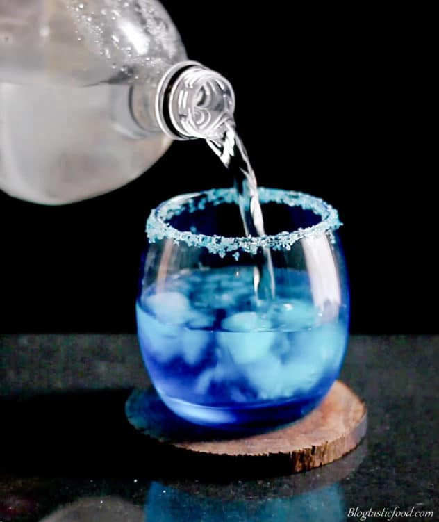 A photo of lemonade being poured into a glass filled with ice, blue curacao and vodka.