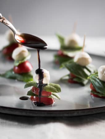 A photo of balsamic glaze being drizzled over mini caprese salad skewers.