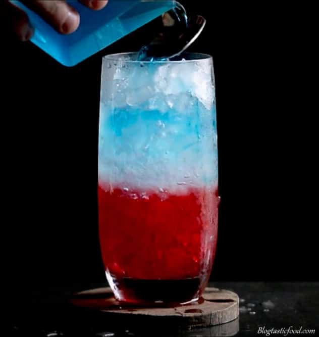 Blue curacoa slowly being poured into a tall glass. 