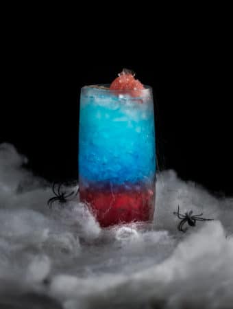 An eye level photo of a spiderman red and blue themed cocktail surrounded by webs.