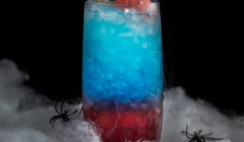 An eye level photo of a spiderman red and blue themed cocktail surrounded by webs.