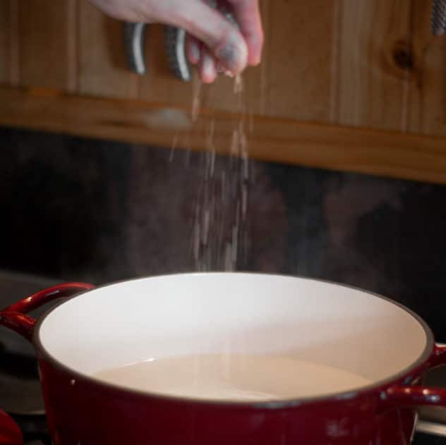 A photo of some sprinkling salt in a pot filled with water. 