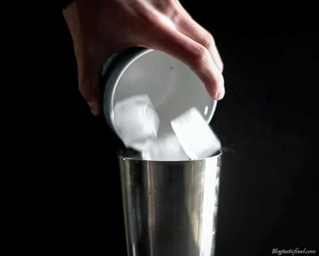 A photo of ice cubes being added to a cocktail shaker. 