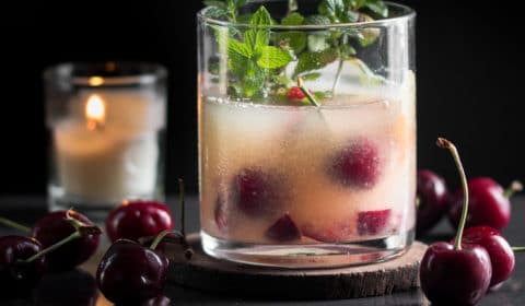 An orange whiskey sour garnished with cherries and mint.