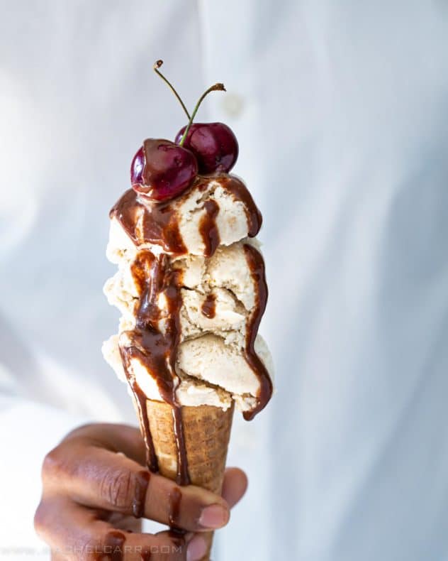 Coconut Ice cream served in a cone with chocolate sauce dripping over it.