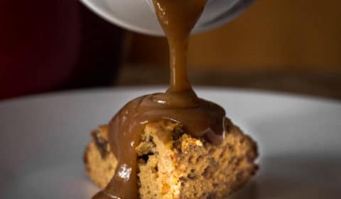 A photo of butterscotch sauce being poured over sticky date pudding.