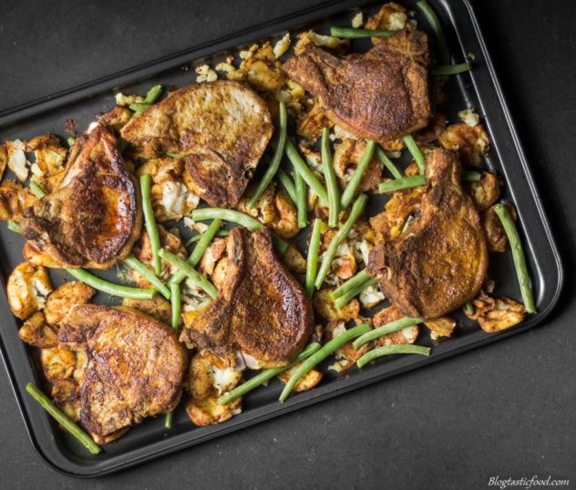 An overheaf photo of baked, curried pork chops and potatoes with green beans on a tray. 