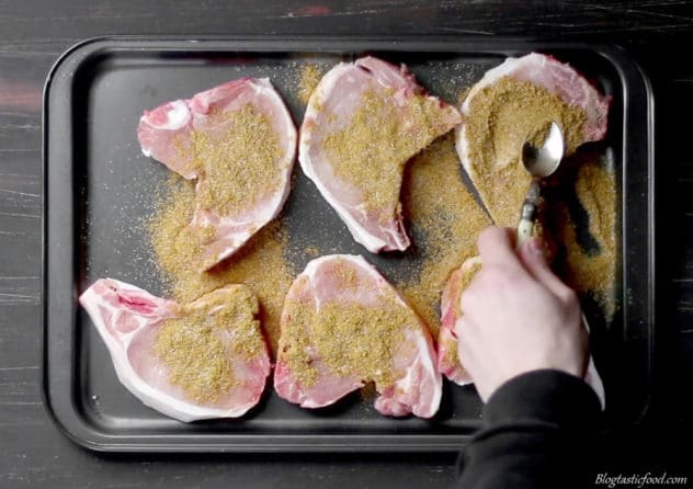 Curry spice being rubbed over pork chops on a tray. 