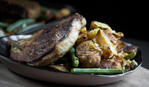 A baked curried sheet pan pork chop, potato and green bean recipe served on a ceramic plate.
