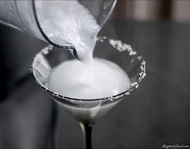 A photo a frozen margarita being transfered from a blender to a cocktail glass.