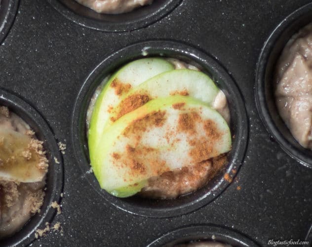 A photo of sliced apples fanned over muffin batter with cinnamon sprinkled on top.