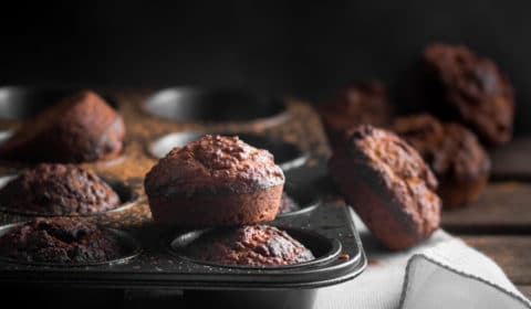 A muffin tray, oatmeal muffins and a white cloth in a wooden surface.