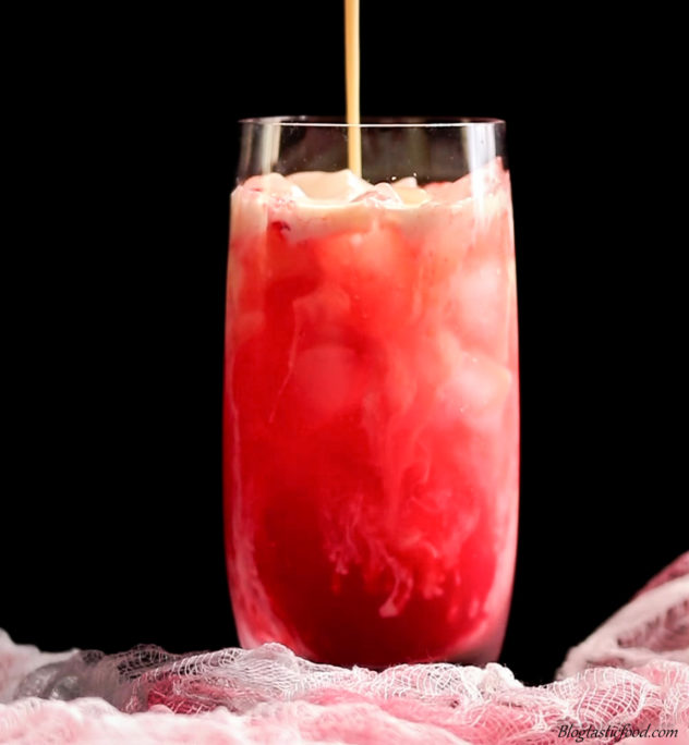 A photo of melted ice-cream slowly being poured into a blood orange cocktail.