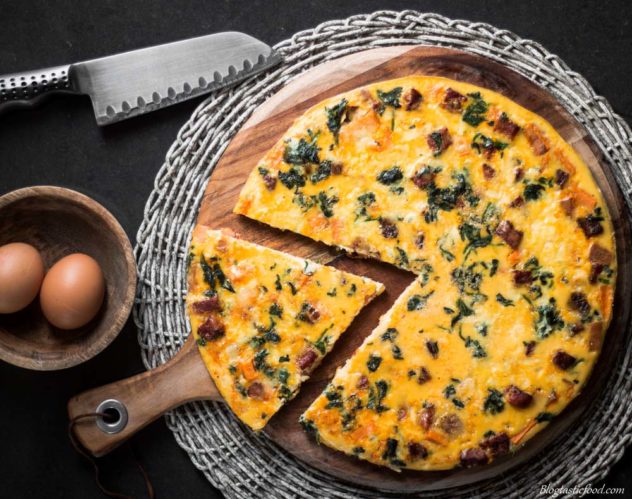 An overhead photo of a frittata served on a wooden circle board.