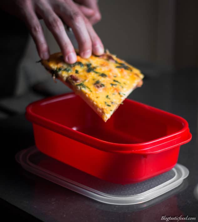 A photo of a slice of frittata being placed in a red container.