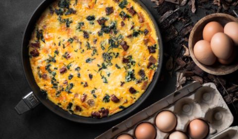 An overhead photo of a frittata in a pan next to a dozen eggs.