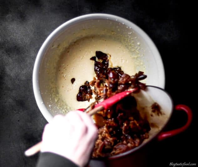 A cooled date mixture being added to pudding batter.