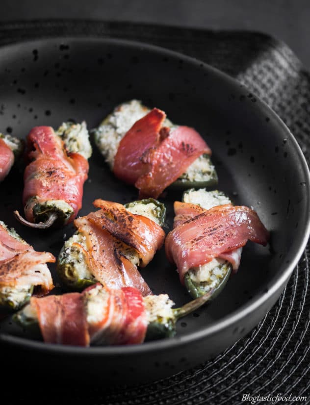 Bacon wrapped baked stuffed jalapenos served in a black bowl.