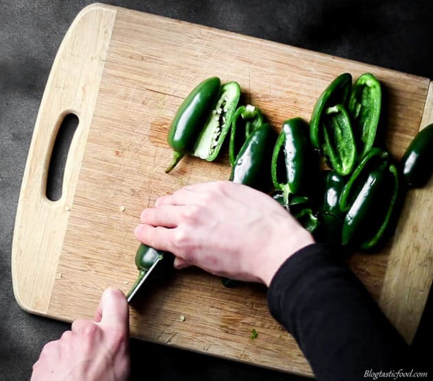 A photo of jalapenos being cut in half lengthways on a board.