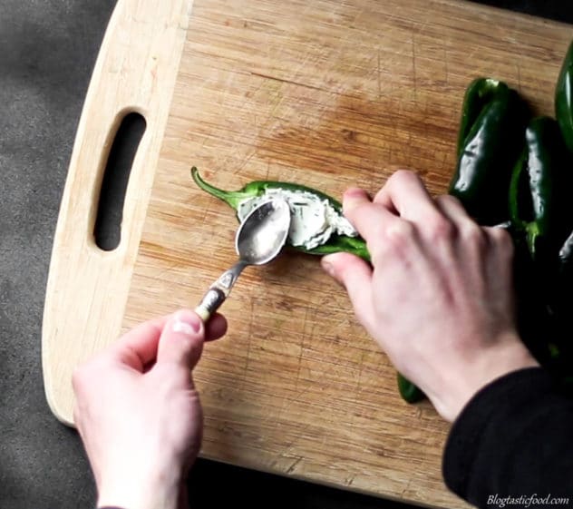 A photo of halved jalapenos being stuffed with a parsley and cream cheese mixture.