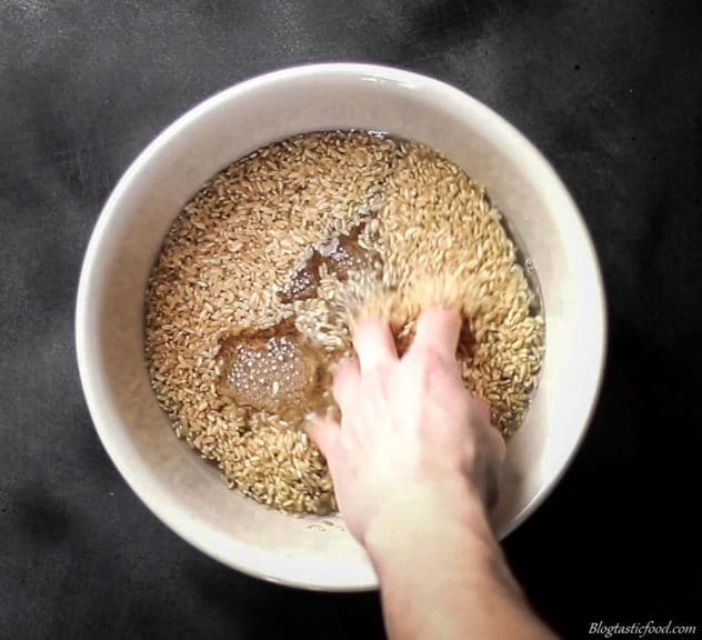 Someone putting there hand in a bowl of soaking brown rice.