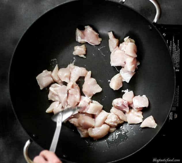 An overhead photo of diced chicken frying in a wok.