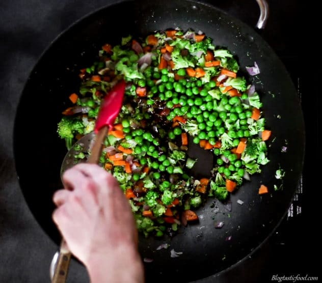 A photo of vegetables, soy sauce and hoisin sauce being stirred in a hot wok.