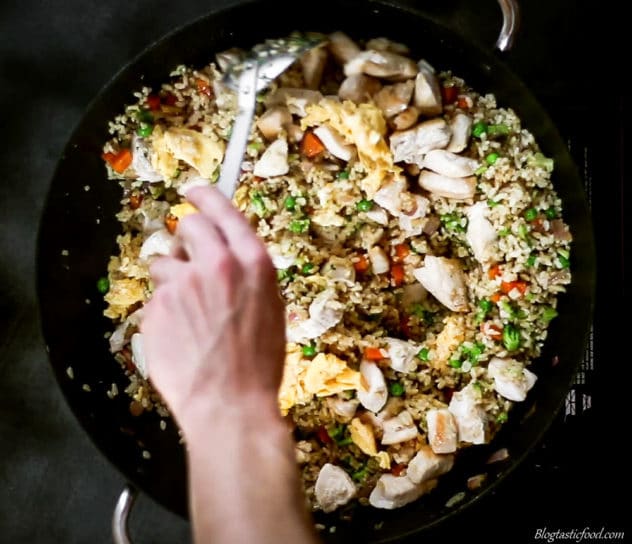 A photo of brown fried rice filled with chicken, egg and vegetables being stirred in a wok.
