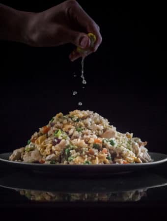 Lime juice being squeezed on top of a pile of brown fried rice.