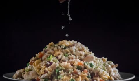 Lime juice being squeezed on top of a pile of brown fried rice.