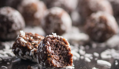 A photo of a group of protein balls on a black surface, with shredded ccocnut scattered everywhere.