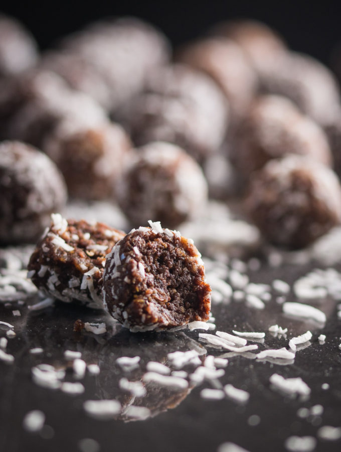 A photo of a group of protein balls on a black surface, with shredded ccocnut scattered everywhere.
