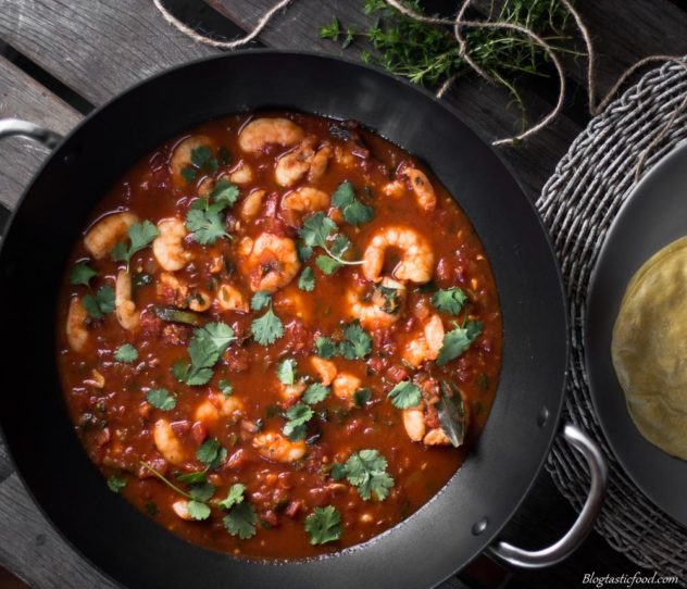 An overhead photo of prawn Rougaille in a work, with fresh thyme and some dhal puri on the side.